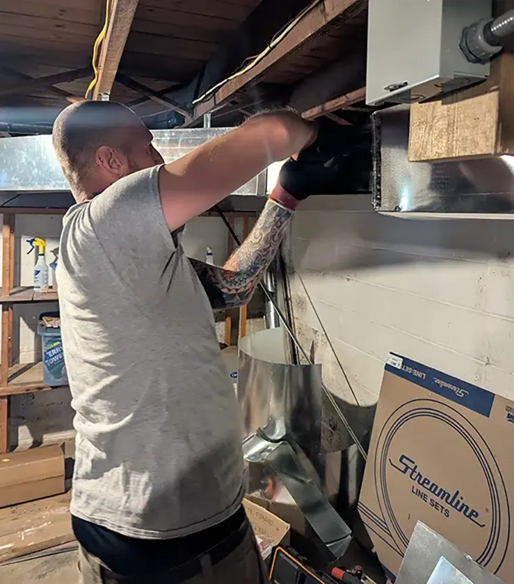 Technician installing HVAC ductwork in a Cherry Hill basement for Davis Heating and Air